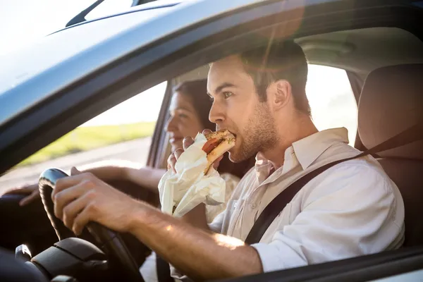 guy eating and driving in the car with his girlfriend in passenger seat