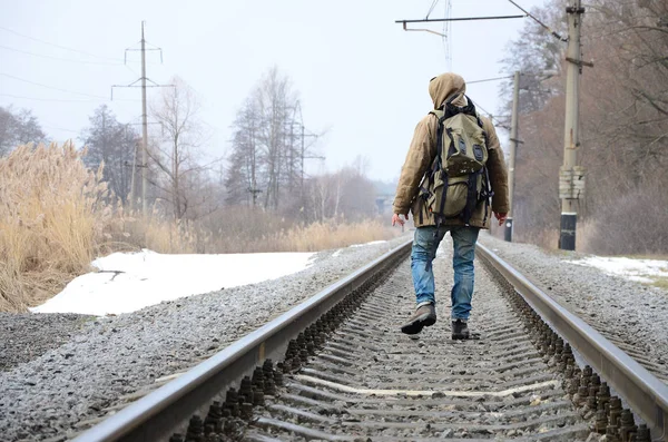 Man with backpack walking in middle of railroad tracks